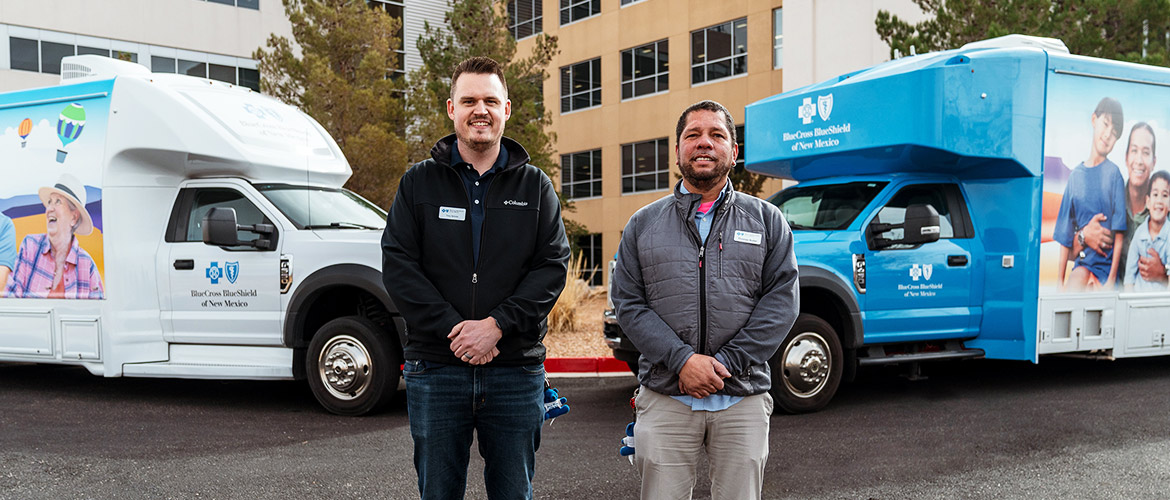 Two men stand before two mobile health vans